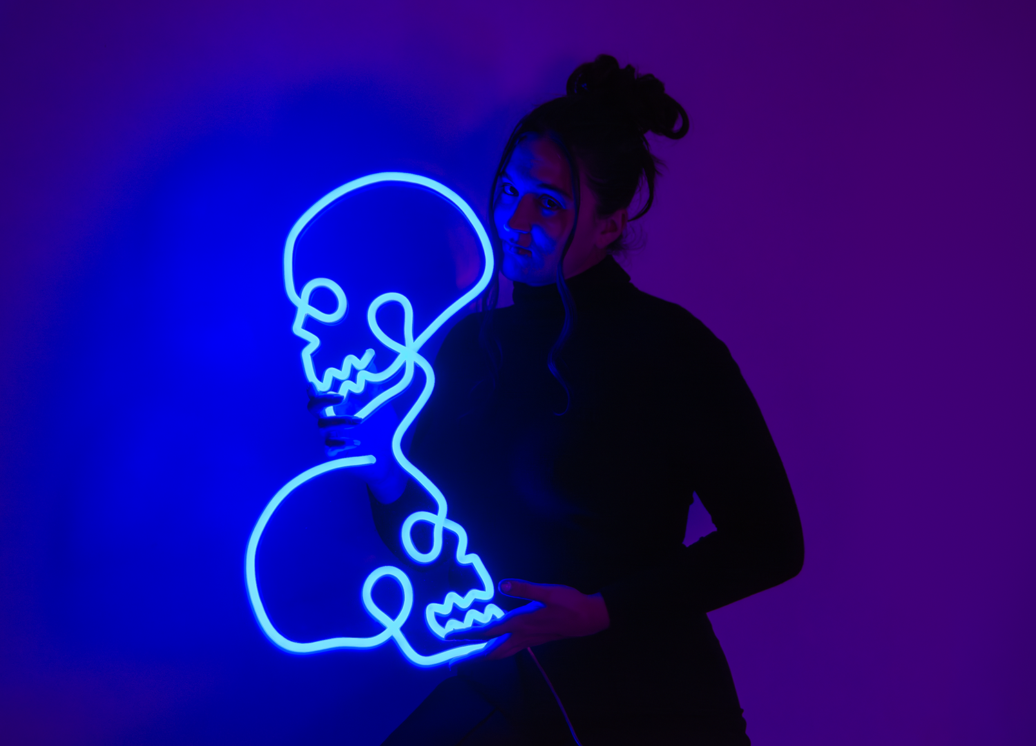 Girl holding a blue neon sign of two skulls