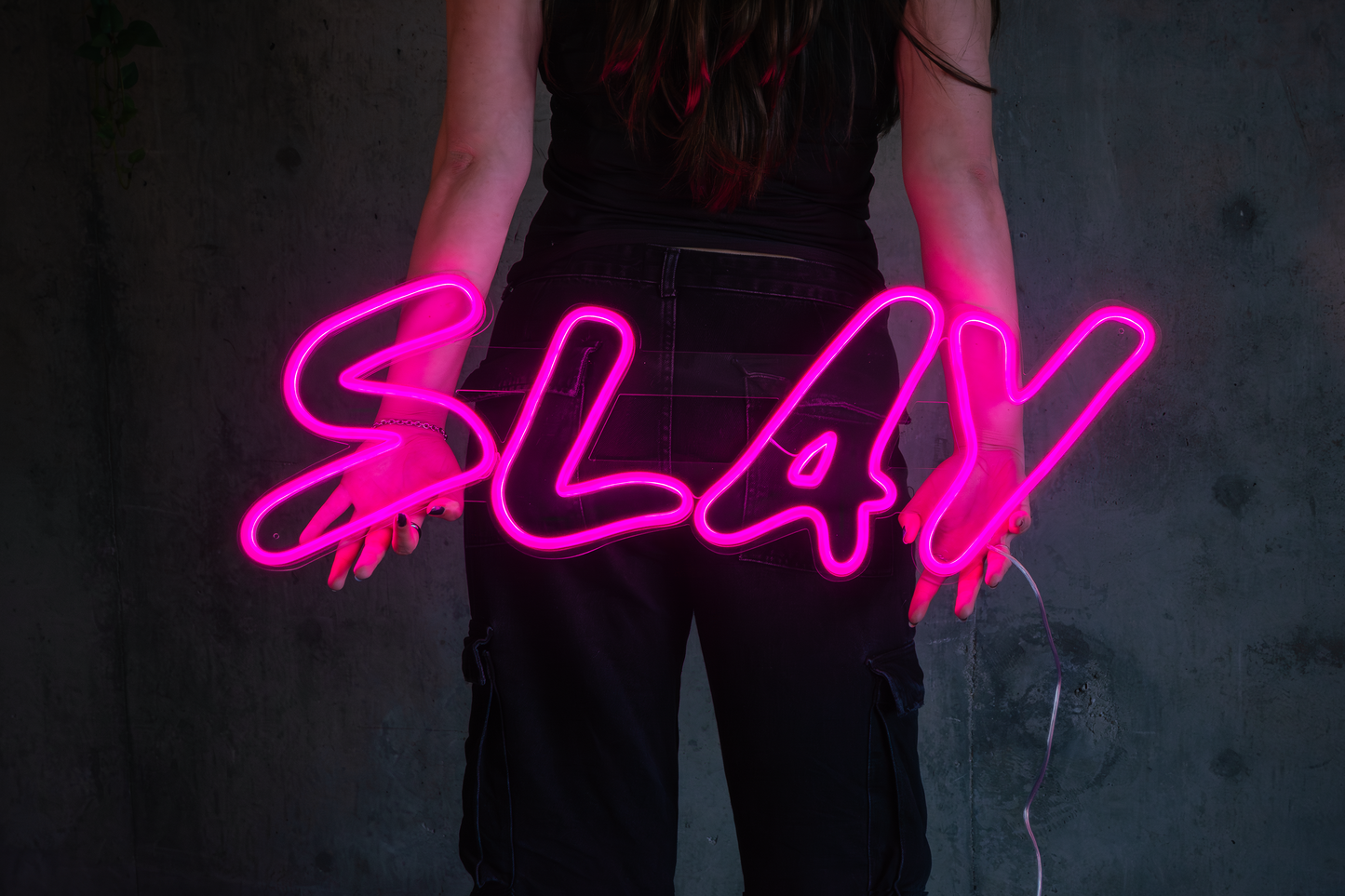A girl holding backwards a pink neon sign that says slay