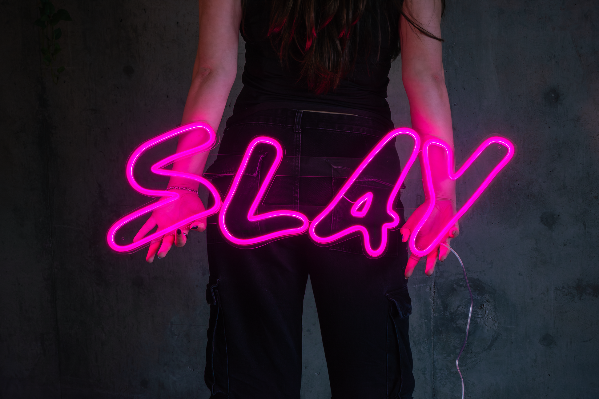 A girl holding backwards a pink neon sign that says slay