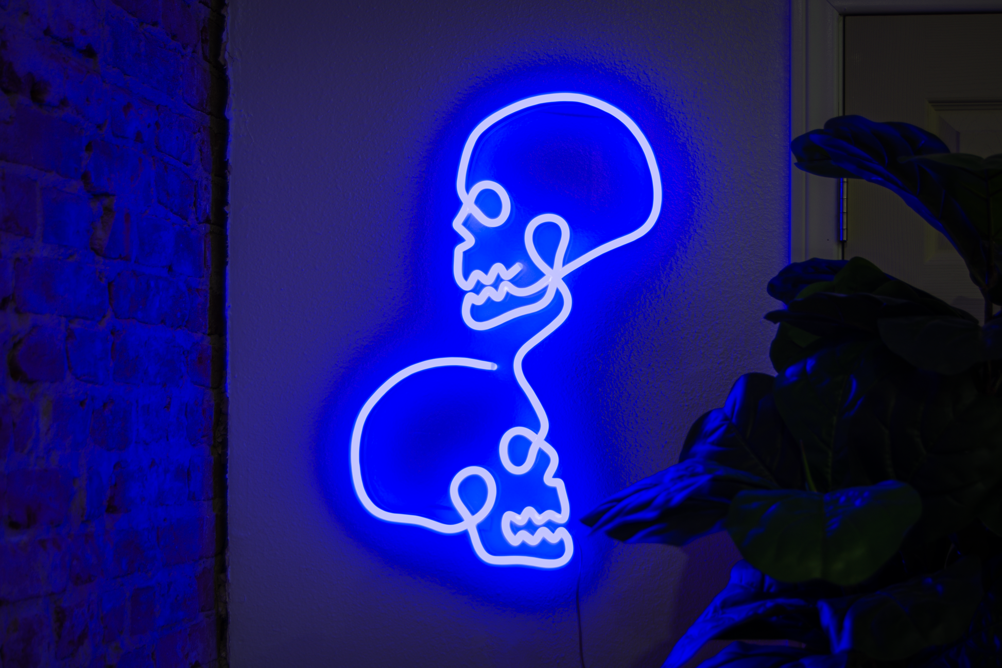 A blue neon sign of two skulls hung up next to a tile wall