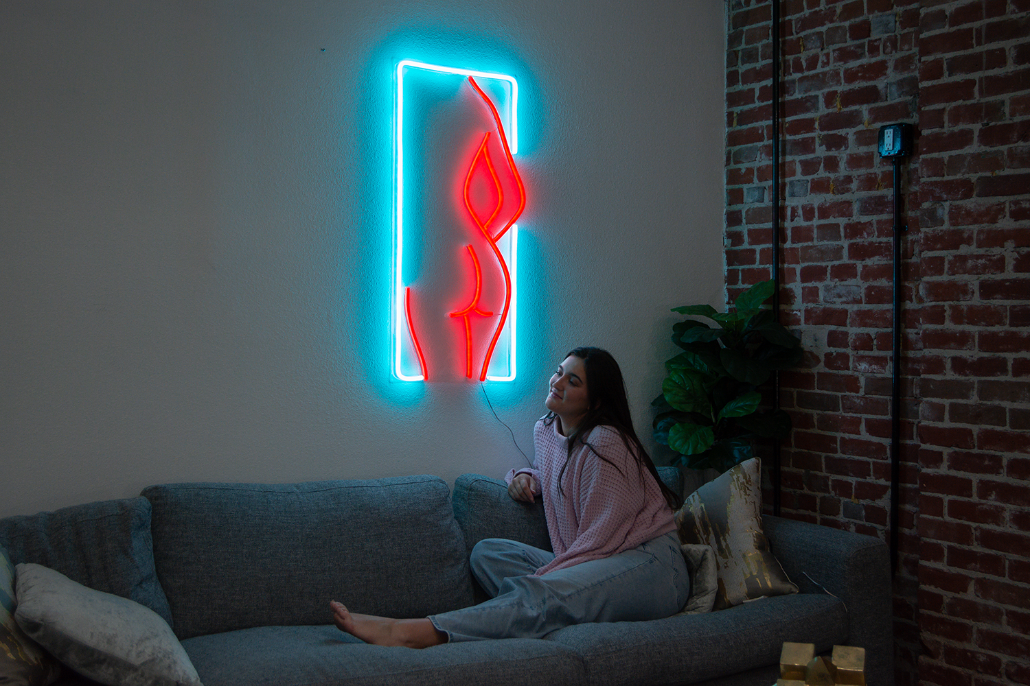A woman sitting on a sofa, next to a blue and red neon sign of a female silhouette