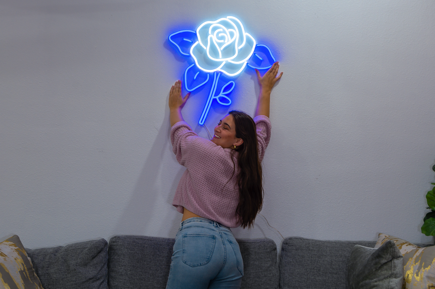 A beautiful girl reaching for a blue and white neon sign of a flower.