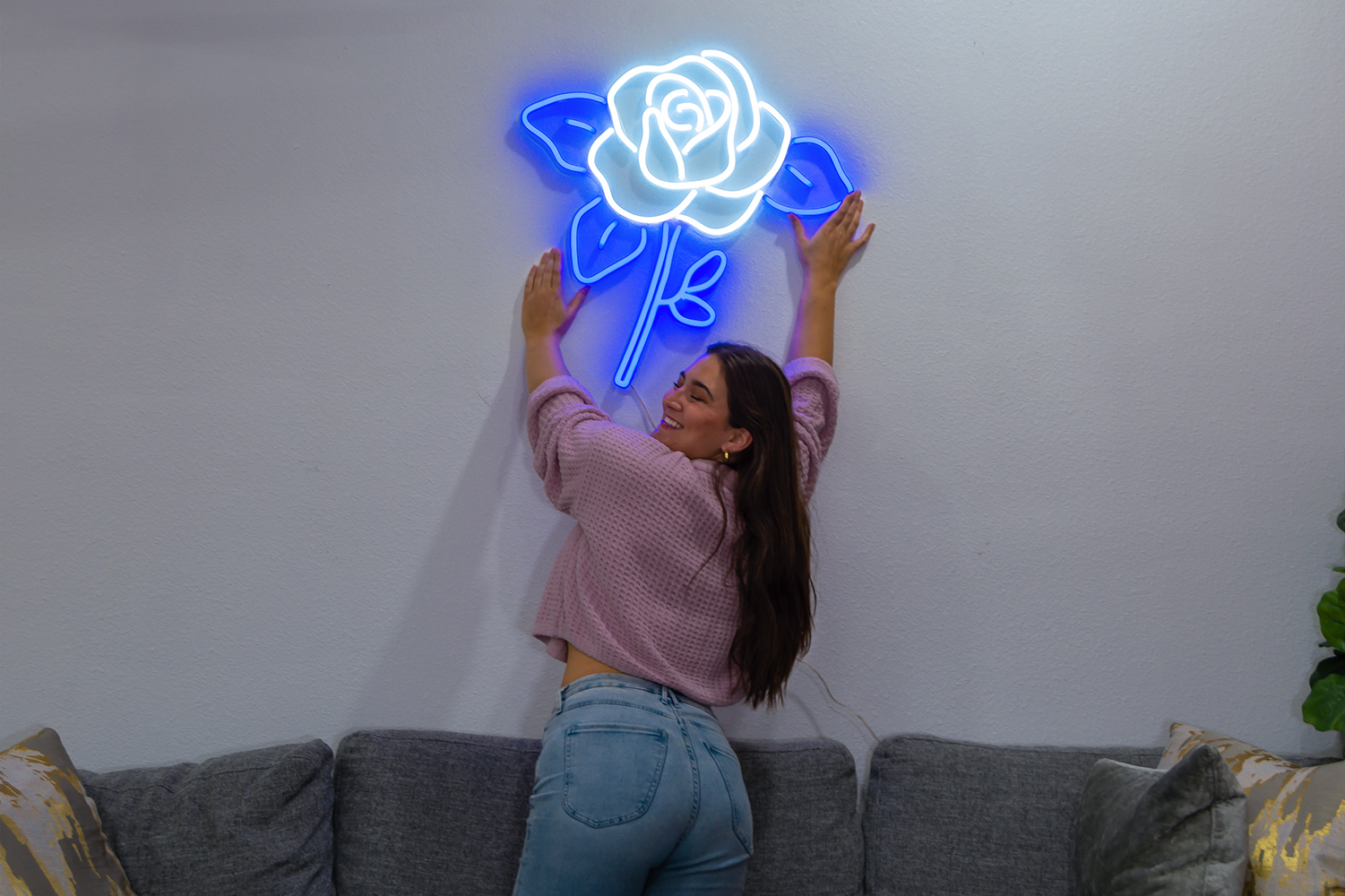 A beautiful girl reaching for a blue and white neon sign of a flower.