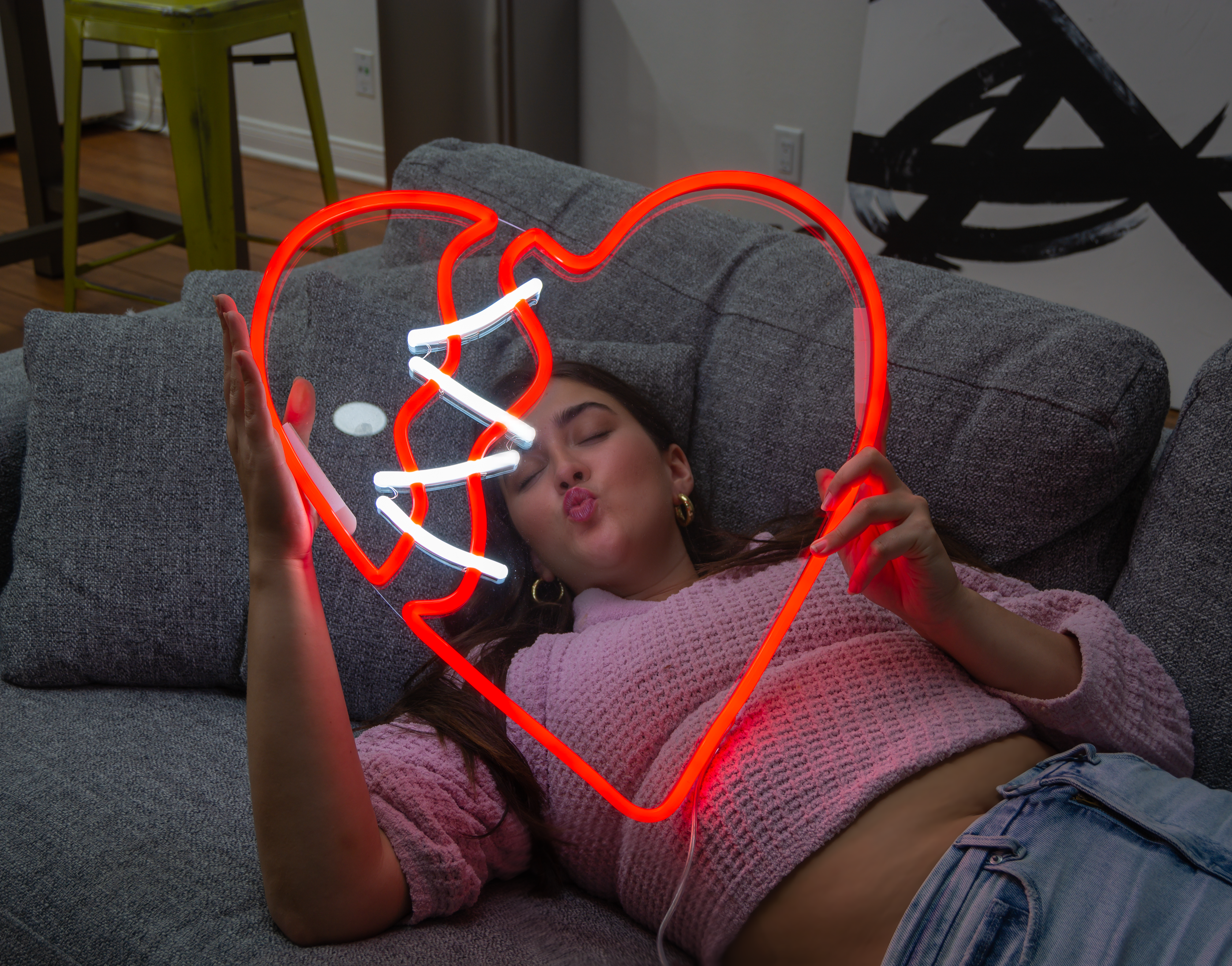 A woman holding a red neon sign of a broken heart.