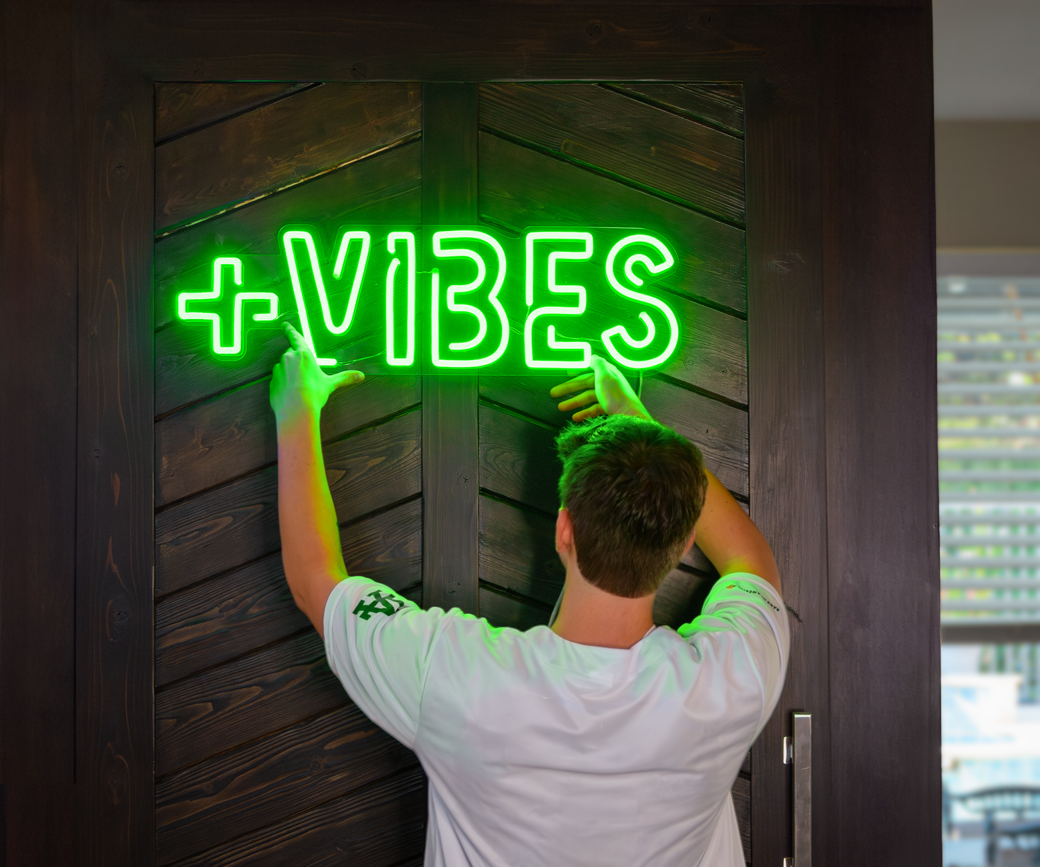 a man holding a green neon sign that says "positive vibes"