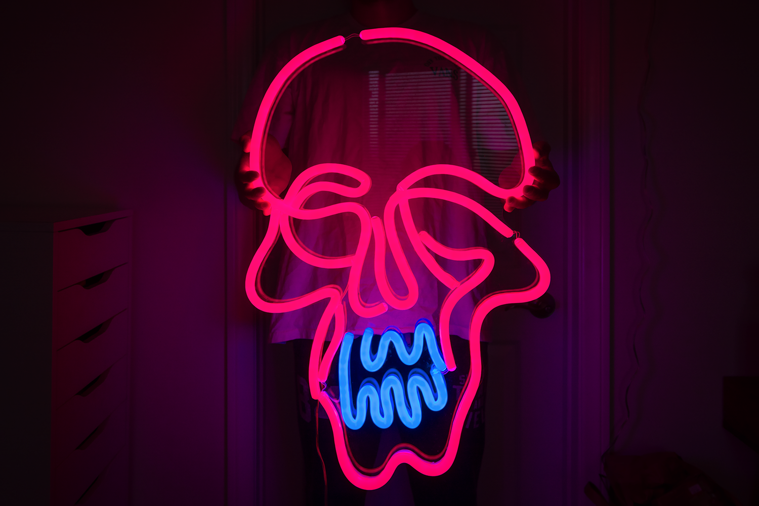 A person holding a large, pink and blue neon sign. The neon sign depicts an artistic skull.