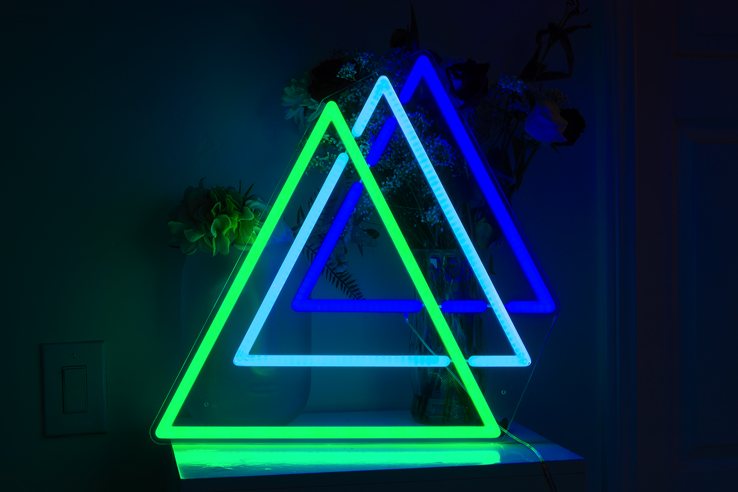 A green and blue neon sign of three triangles