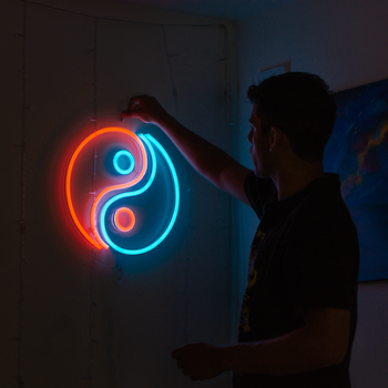 A man standing in a dark room in front of a yin and yang neon sign that is orange and light blue.