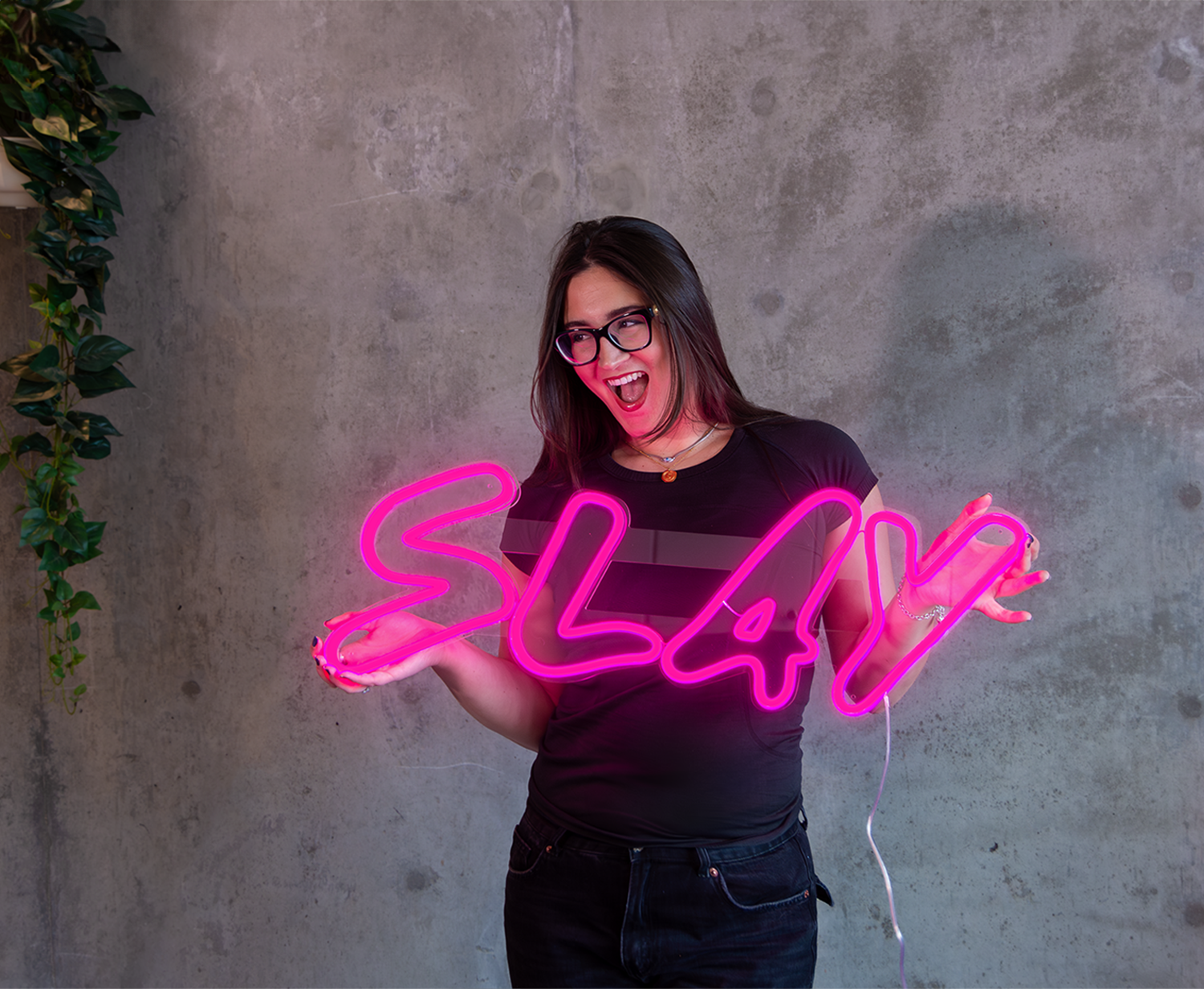 Girl holding a pink neon sign that says "slay"