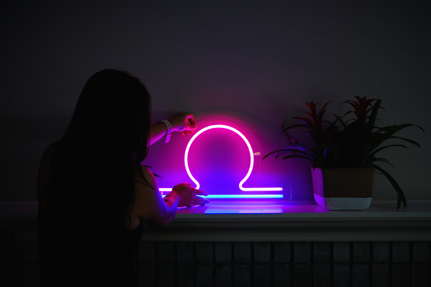 A woman admiring her libra zodiac neon sign. The neon sign is pink and blue.