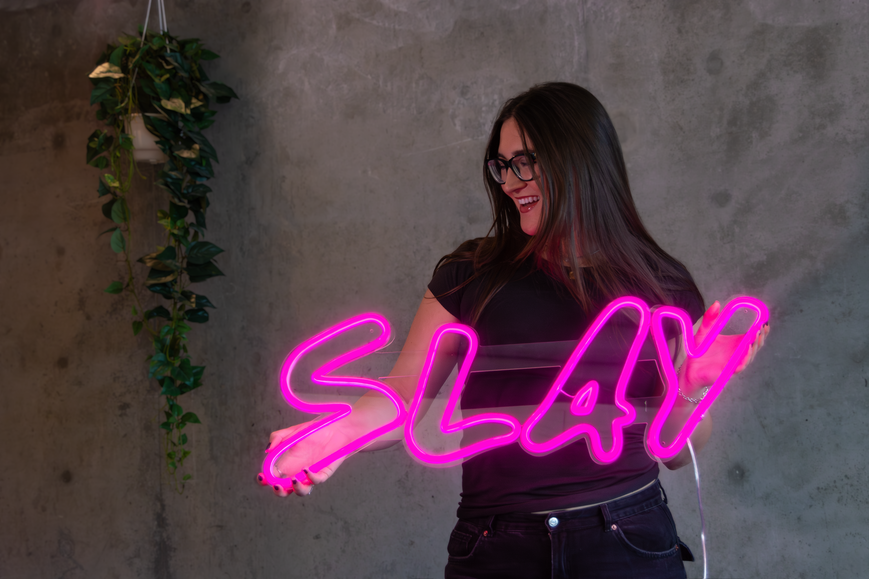a girl holding a pink neon sign that says "slay"