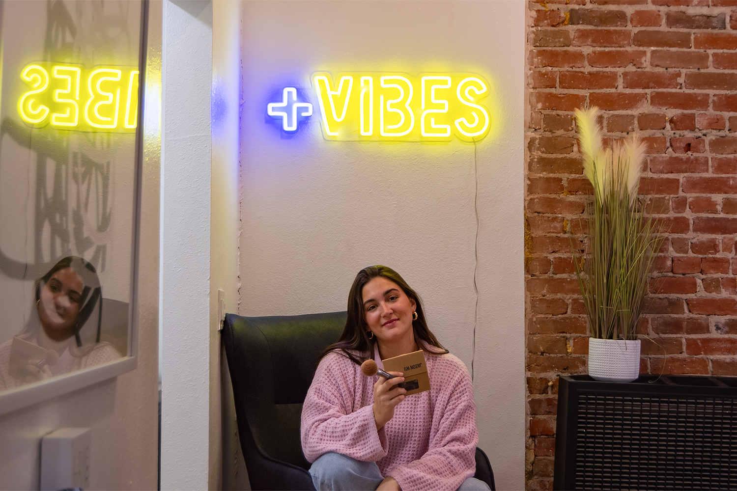 A girl sitting in a chair under a neon sign that says "positive vibes".